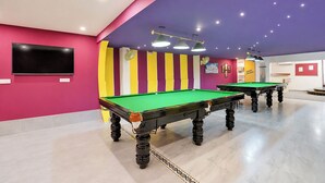 Zona de mesas de billar con dos mesas, un televisor de pantalla plana y un cartel que dice 'Game Lounge'.