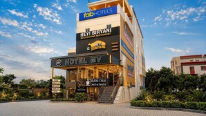 Un hotel de varios pisos con un cartel que dice 'Hotel MV' y un restaurante llamado 'Hey! Biryani Multicuisine Restaurant' en el nivel superior.