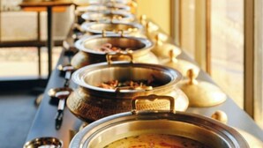 Una barra de buffet con varios platos en recipientes metálicos.