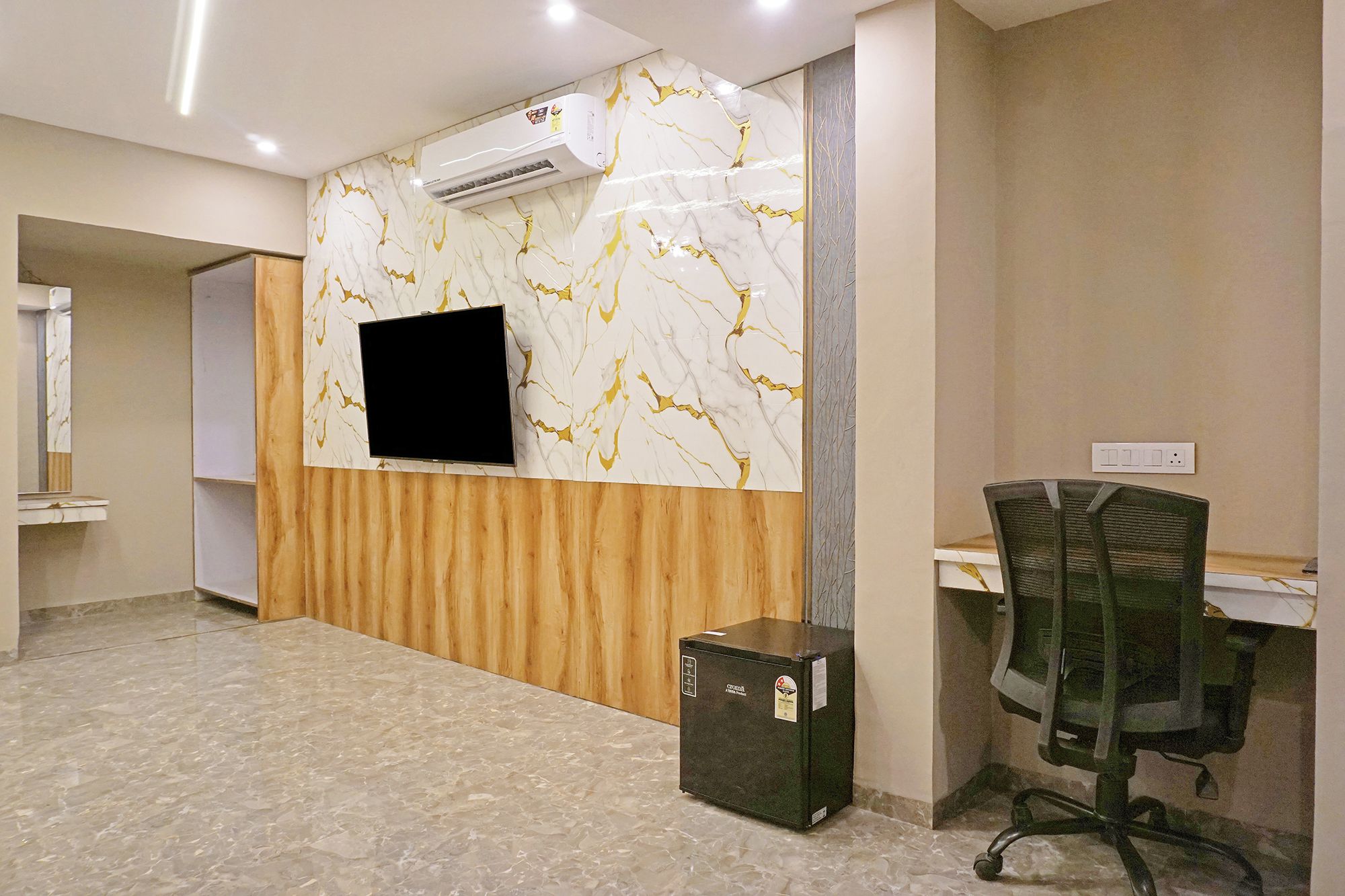 Un área de recepción con pared de mármol, televisor montado, escritorio de madera y silla de oficina negra.