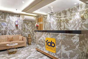 A hotel reception area with a marble wall, a sofa, a coffee table, a vase with flowers, a clock, and a sign for 'fab hotels'. - Fabhotel Nest Inn (Mumbai)