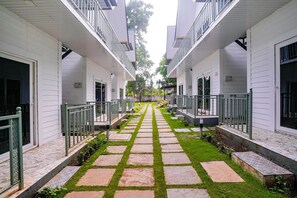 A corridor with a central pathway flanked by white buildings, each with a balcony and a door.