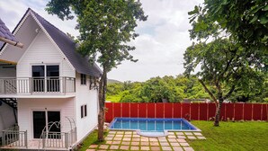 A two-story house with a swimming pool, a red fence, and a paved patio area. - FabHotel Hill View Cottages (Arpora)