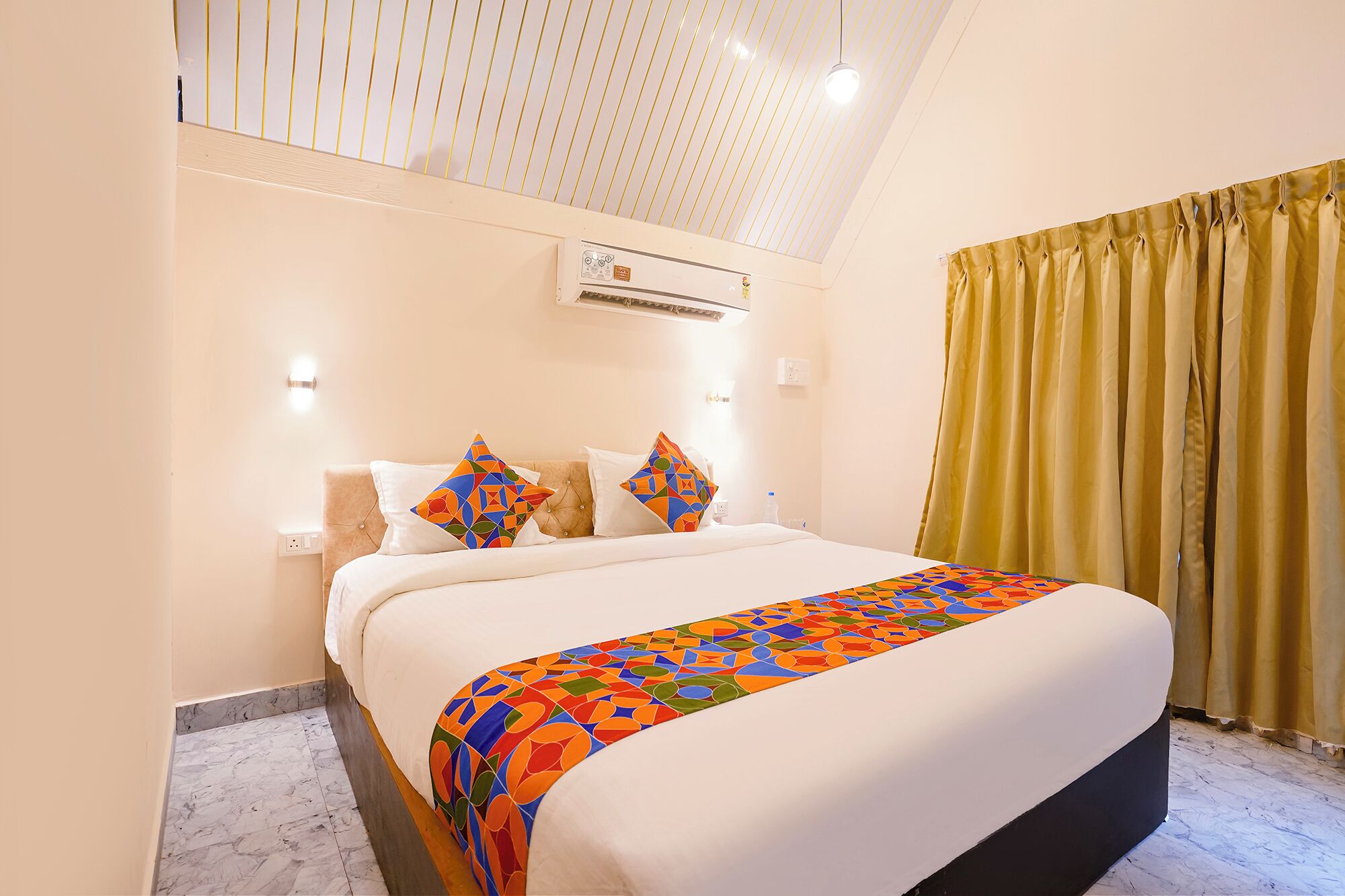 Habitación de hotel con una cama, cabecero, unidad de aire acondicionado, ventana con cortinas y suelo de mármol.