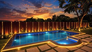 Una piscina con bordo piastrellato, circondata da una recinzione in legno e un albero.