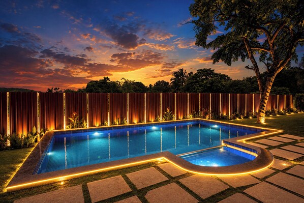 A swimming pool with a tiled edge, surrounded by a wooden fence and a tree.
