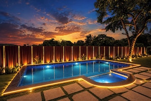 Una piscina con borde de azulejos, rodeada por una valla de madera y un árbol.