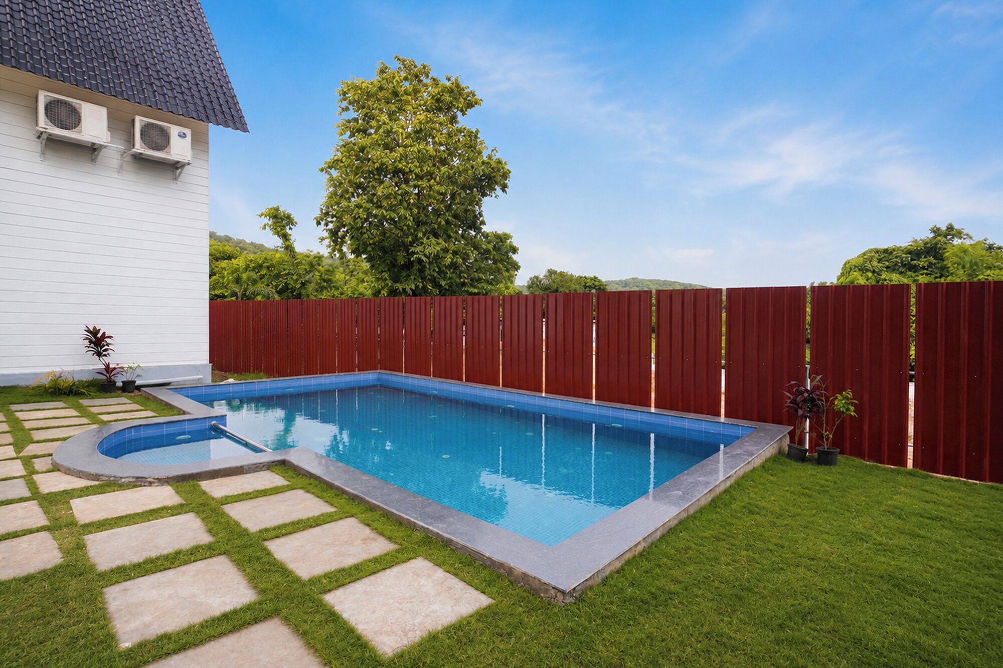 A rectangular swimming pool with a tiled edge, surrounded by a red fence, and a grassy area with stepping stones leading to the pool.