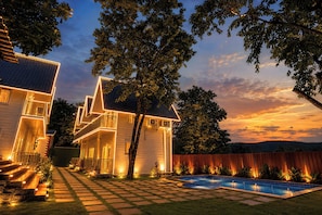 Una casa de dos pisos con piscina, rodeada de árboles y una cerca de madera.
