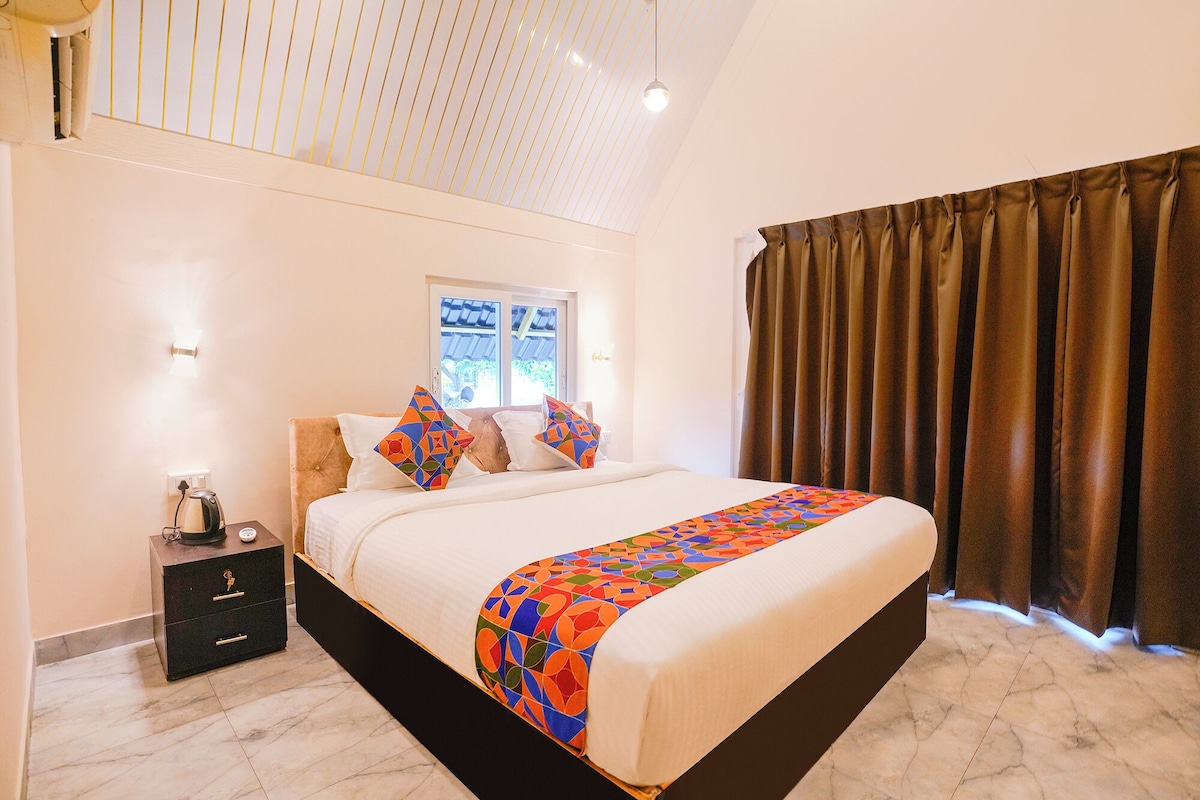 Una habitación de hotel con una cama, una mesita de noche, una lámpara y un ventanal con cortinas.