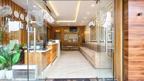 A reception area with a glass partition, wooden paneling, a reception desk, a seating area, and a television mounted on the wall. - Fabhotel Shubh Mangal Grand (Gwalior)