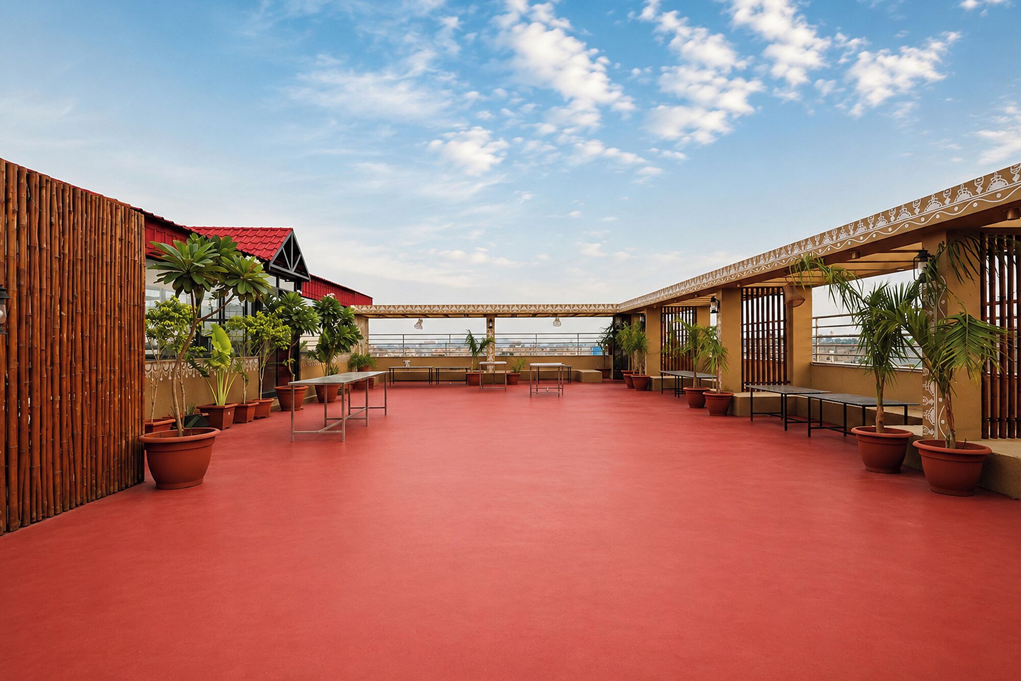 Una terraza en la azotea con piso rojo, plantas en macetas y vistas de la ciudad.