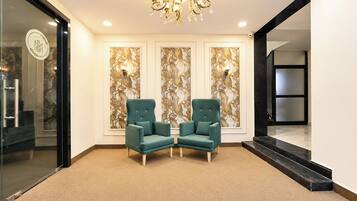Un hall con dos sillones color turquesa, un revestimiento de pared con diseño de mármol, una araña y una puerta de cristal con un logotipo.