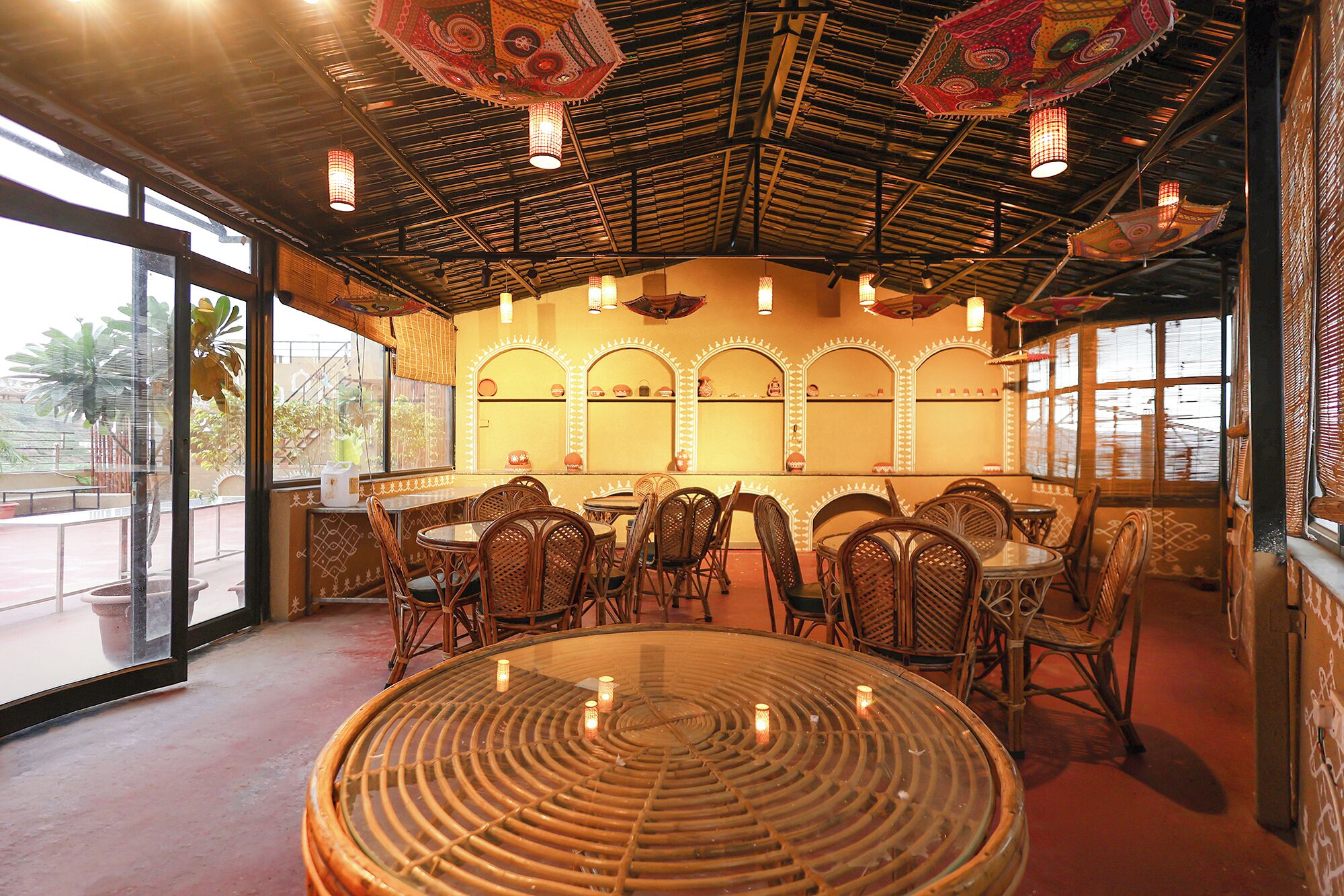 Un interior de restaurante con mesas redondas, sillas de mimbre y lámparas decorativas en el techo.
