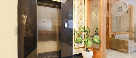A modern elevator with a digital display, a potted plant, and a reception area with a couch and a sign.