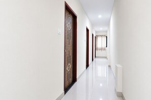 A corridor with doors on both sides, a tiled floor, and a radiator on the right. - Via Nutan Lodging (Pune)