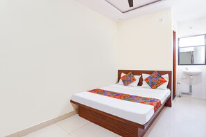 A bedroom with a wooden bed frame, white bedding, and colorful geometric pillows. - Via Nutan Lodging (Pune)