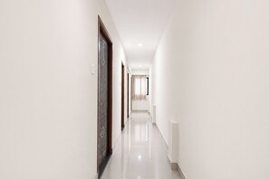 A long, narrow hallway with white walls and a glossy floor. - Via Nutan Lodging (Pune)
