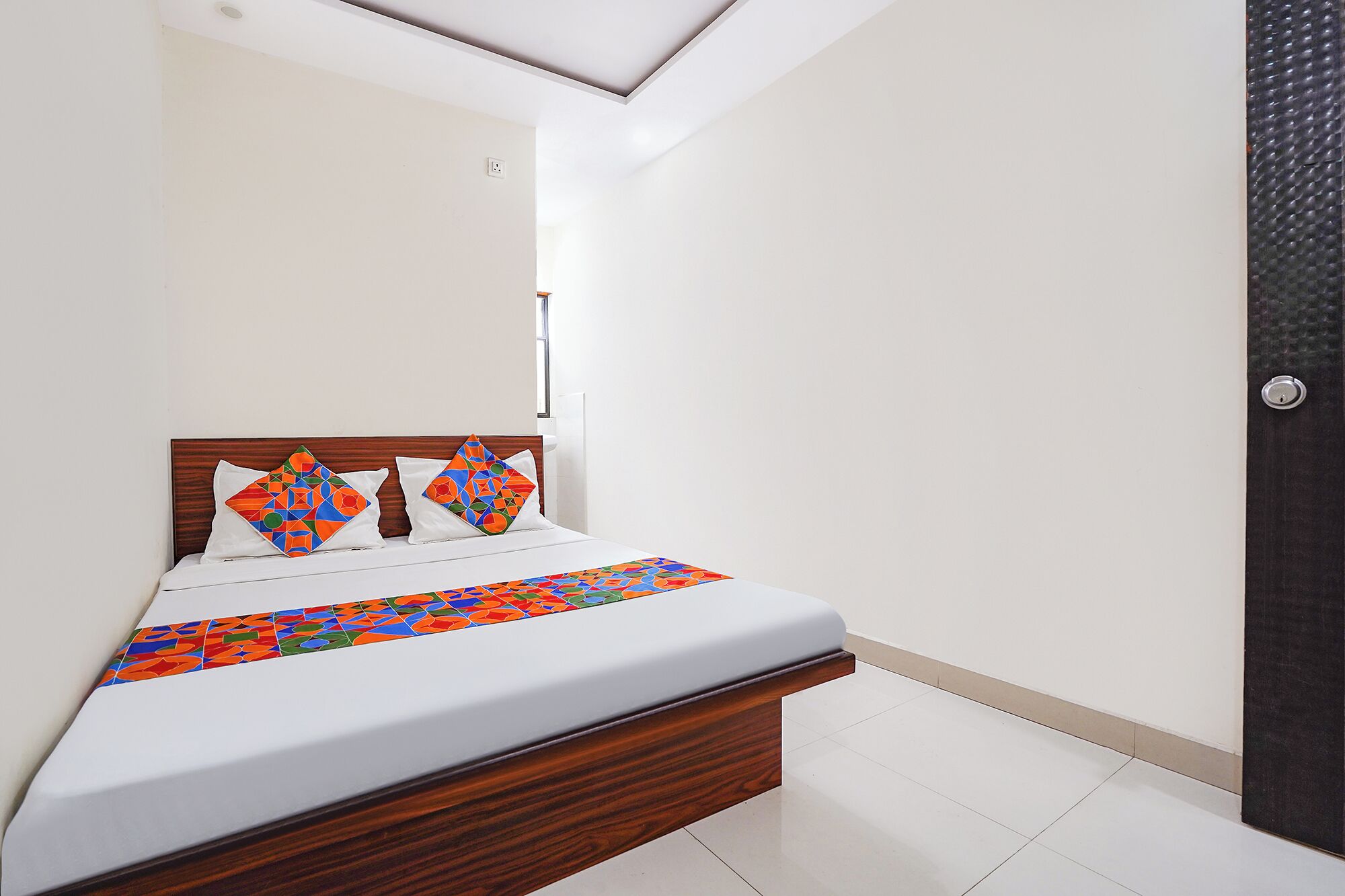A neatly made bed with a wooden headboard, white bedding, and colorful geometric-patterned pillows.