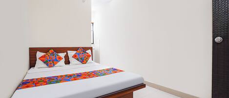 A neatly made bed with a wooden headboard, white bedding, and colorful geometric-patterned pillows.