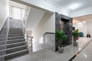 A modern interior with a marble staircase, a reception area, and a seating area with a teal sofa. - Fabhotel Blue Birds (Bengaluru)