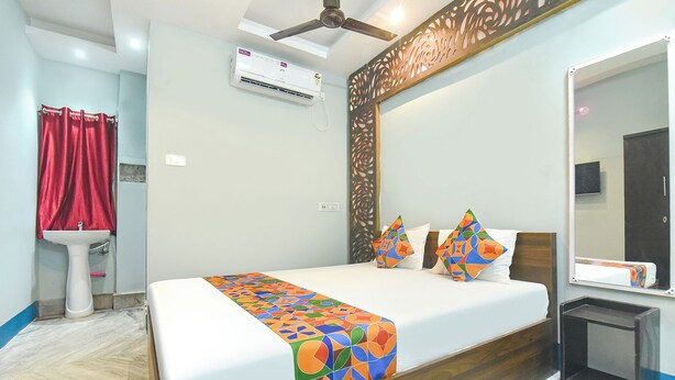 A hotel room with a bed, a bedside table, a mirror, a ceiling fan, an air conditioning unit, and a small cabinet. - Fabhotel Taj Palace (Kolkata)