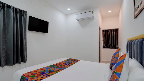 A hotel room with a single bed, a flat-screen TV mounted on the wall, an air conditioning unit, and a door leading to another room. - Fabhotel Seton (Hyderabad)