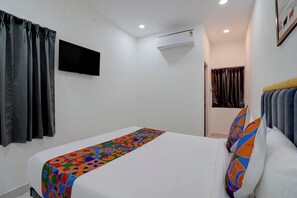 Habitación de hotel con una cama individual, un televisor de pantalla plana montado en la pared, un aire acondicionado y una puerta que da a otra habitación.
