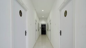 A corridor with white walls and doors, leading to a black door at the end. - Fabhotel Seton (Hyderabad)