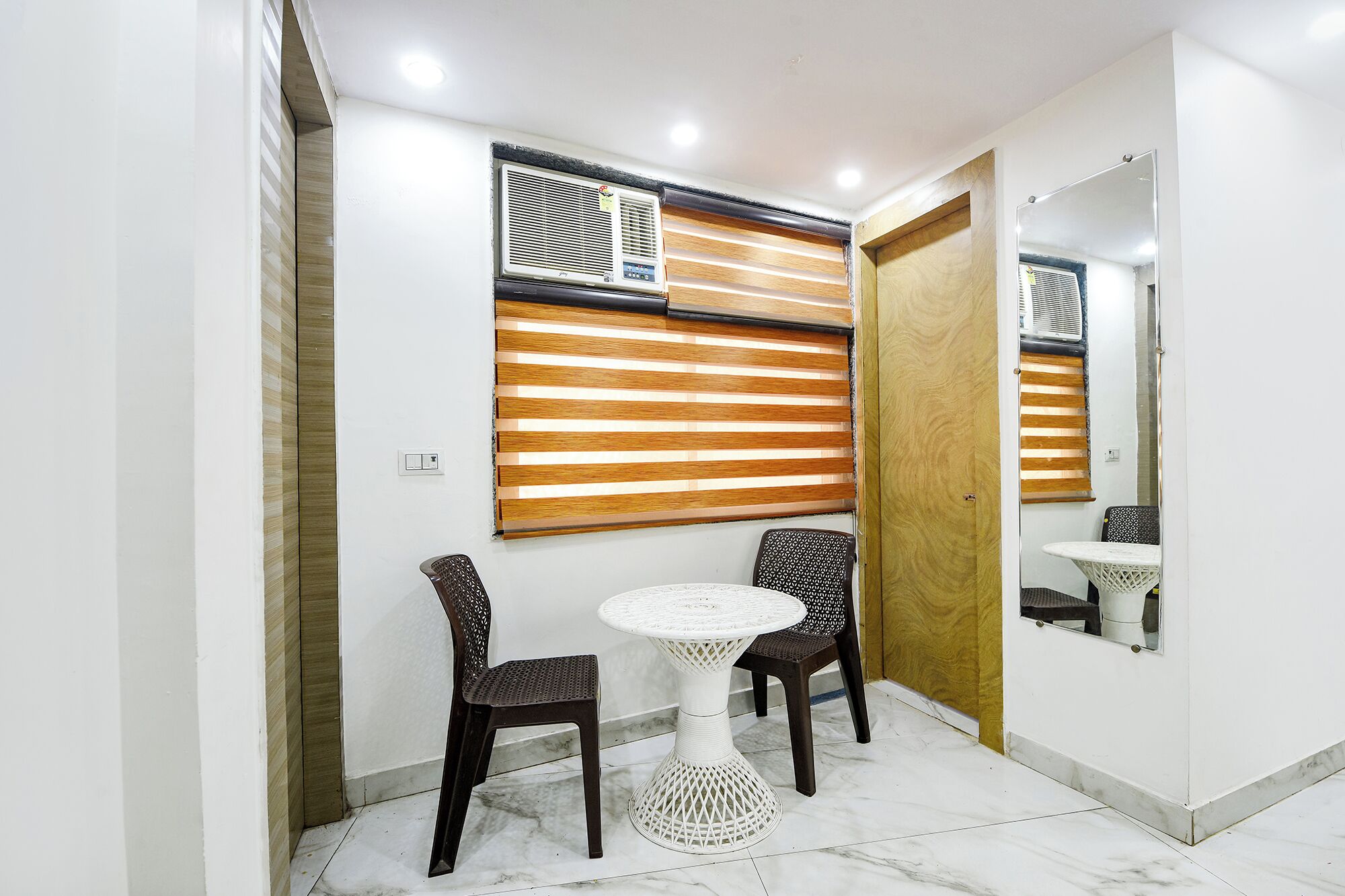 A bathroom with a white tiled floor, two dark brown chairs, a white round table, and a wooden slatted window.