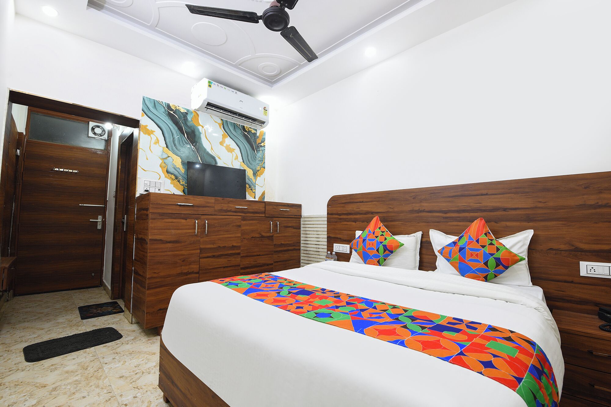 A hotel room with a bed, a wardrobe, a ceiling fan, and an air conditioning unit.
