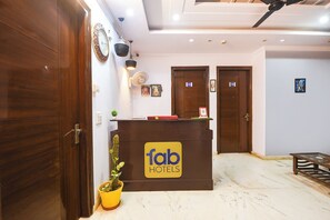 A hotel reception desk with a sign reading 'fab hotels,' a potted plant, and a ceiling fan. - FabHotel Red Flag (Gurugram)