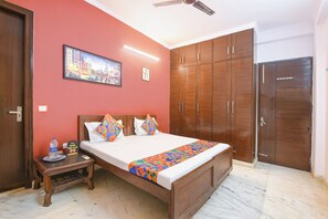A hotel room with a bed, wooden wardrobe, a painting on the wall, and a ceiling fan. - FabHotel Red Flag (Gurugram)