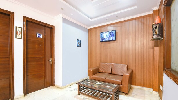 Una habitación con puerta de madera, un sofá de cuero marrón, una mesa de centro de vidrio y un televisor montado en la pared.