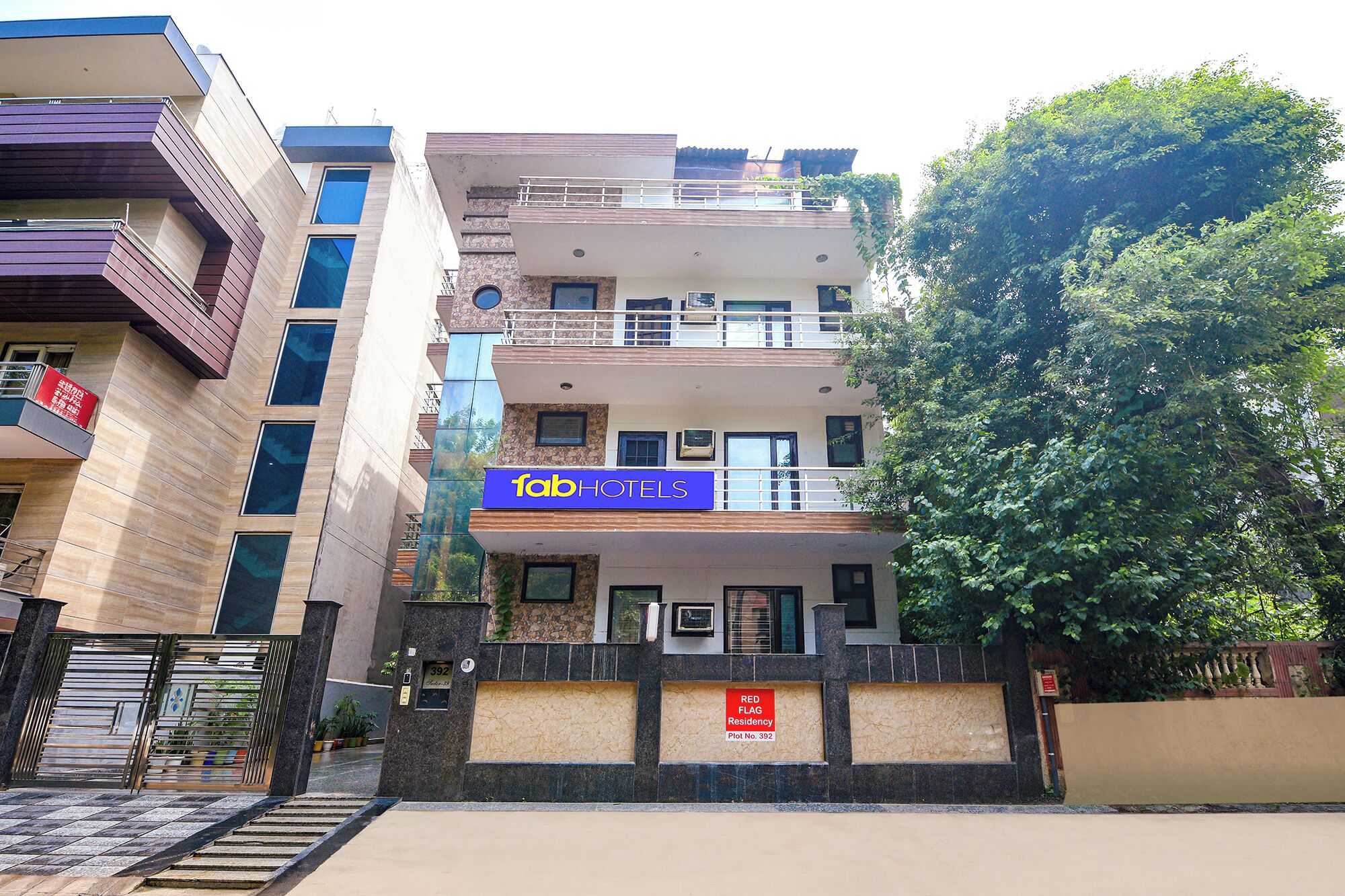 A multi-story hotel with a blue sign reading 'fab HOTELS' and a red flag indicating a residency plot.