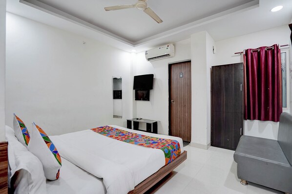 Une chambre à coucher comprenant un lit, un ventilateur de plafond, un appareil de climatisation, une armoire, une petite table et une chaise grise.
