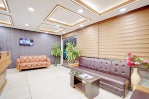 A reception area with a wooden reception desk, a patterned sofa, a leather sofa, a glass coffee table, and a wall-mounted TV. - Fabhotel Saanvi Paradise (Bhopal)