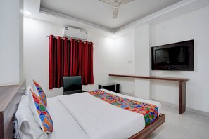 Une chambre d’hôtel avec un lit, un bureau, une chaise, une télévision et une fenêtre avec des rideaux rouges.