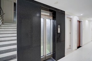 A hallway with a black marble wall, a glass door, and a staircase. - Fabhotel Saanvi Paradise (Bhopal)