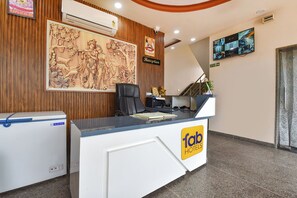 Un mostrador de recepción de hotel con el logotipo de 'fab hotels', una cámara de seguridad, un televisor montado y una pared de madera con un relieve esculpido.