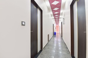 Pasillo de hotel con puertas a ambos lados, techo de patrón rojo y blanco, y un bote de basura azul.
