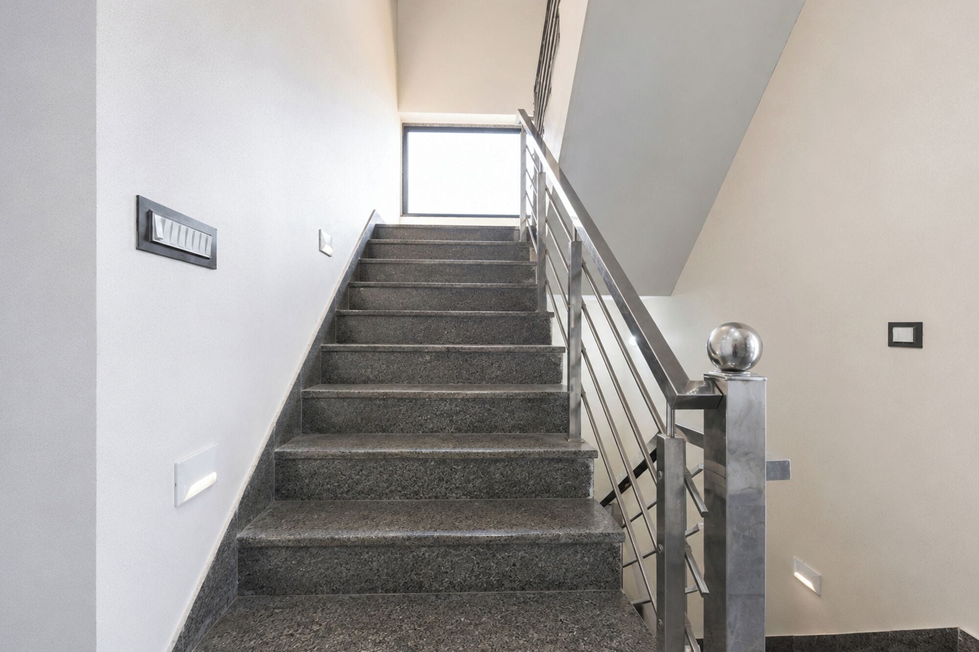 A staircase with a metal railing and a light fixture on the wall.