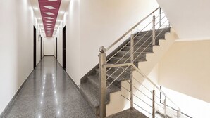 A modern interior with a straight staircase and a hallway leading to a door. - FabHotel Dev Bhumi (Khatoo)