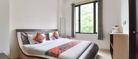 A hotel room with a bed, a window with curtains, a bedside table, and a wardrobe.