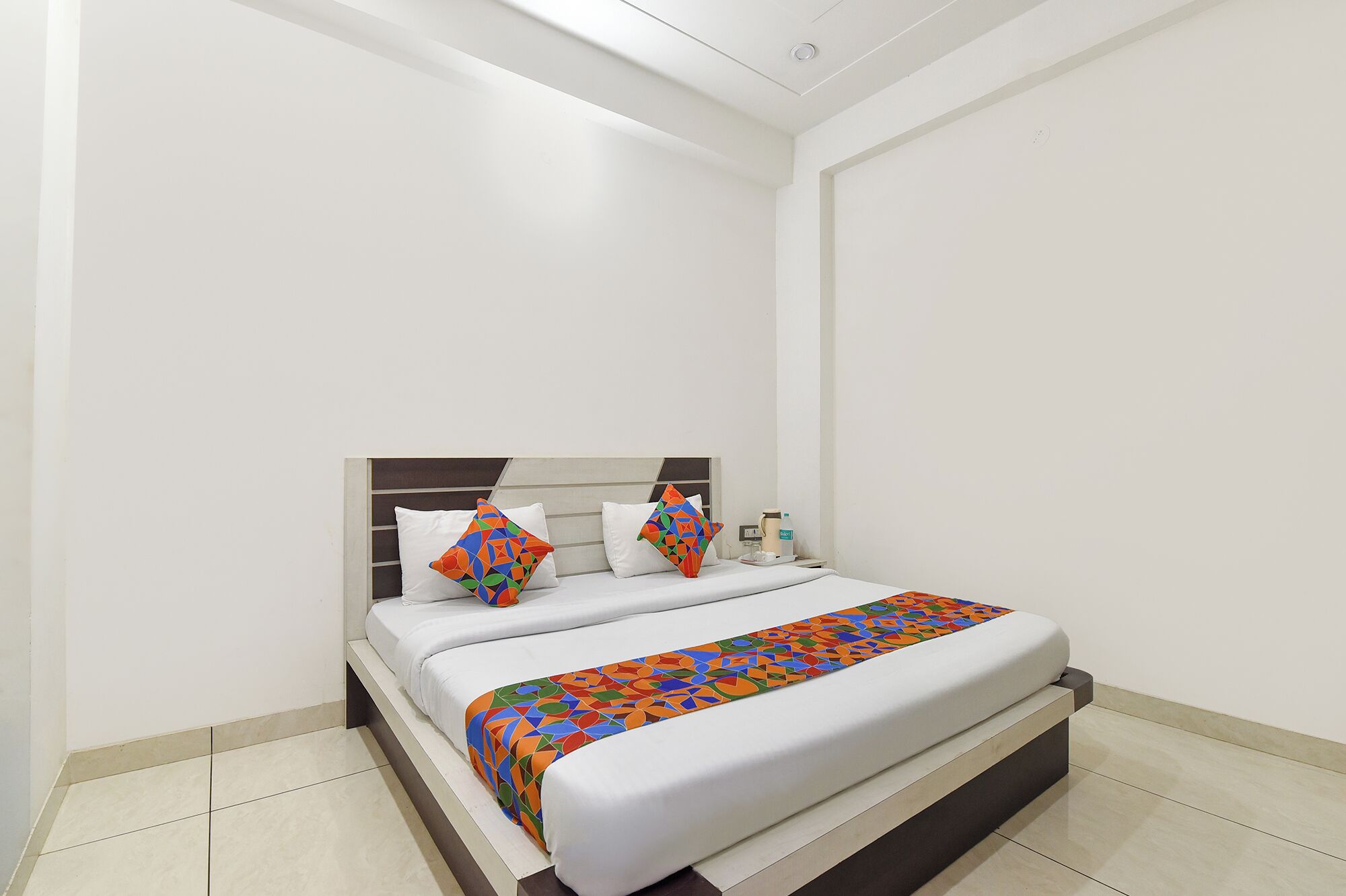Una habitación de hotel con una cama, almohadas y una mesita de noche con lámpara.