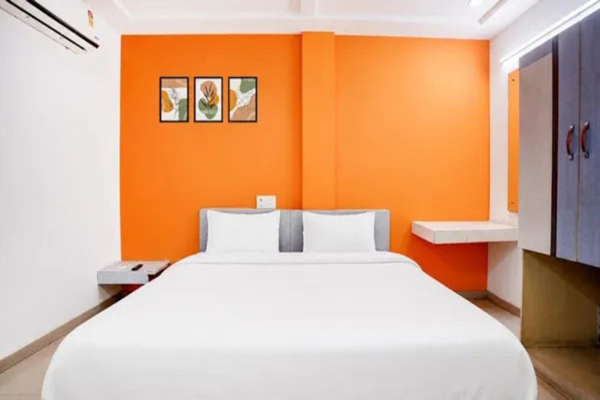 A hotel room with a bed, a nightstand, a dresser, and a wall with three framed pictures.