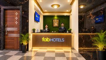 A reception desk with the 'fabHOTELS' logo, two receptionists, a green wall with a framed picture, and potted plants.