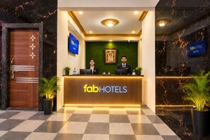 A reception desk with the 'fabHOTELS' logo, two receptionists, a green wall with a framed picture, and potted plants.