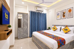 Habitación de hotel con cama, televisión, ventilador de techo y baño con cortina de ducha.
