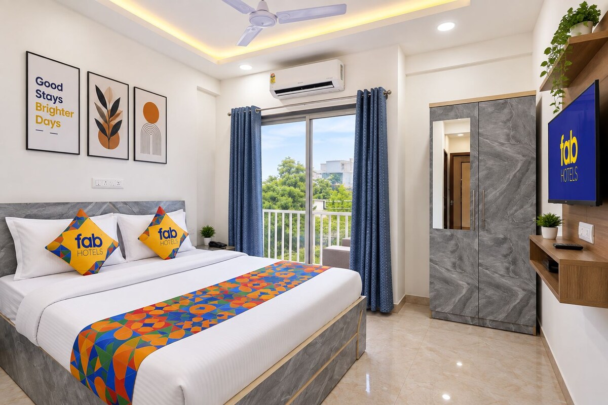 A hotel room with a bed, a TV, a balcony with curtains, and a wall-mounted air conditioner.